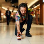 A man with dreadlocks and a colorful T-shirt dropping a cupcake on the floor in a food court.